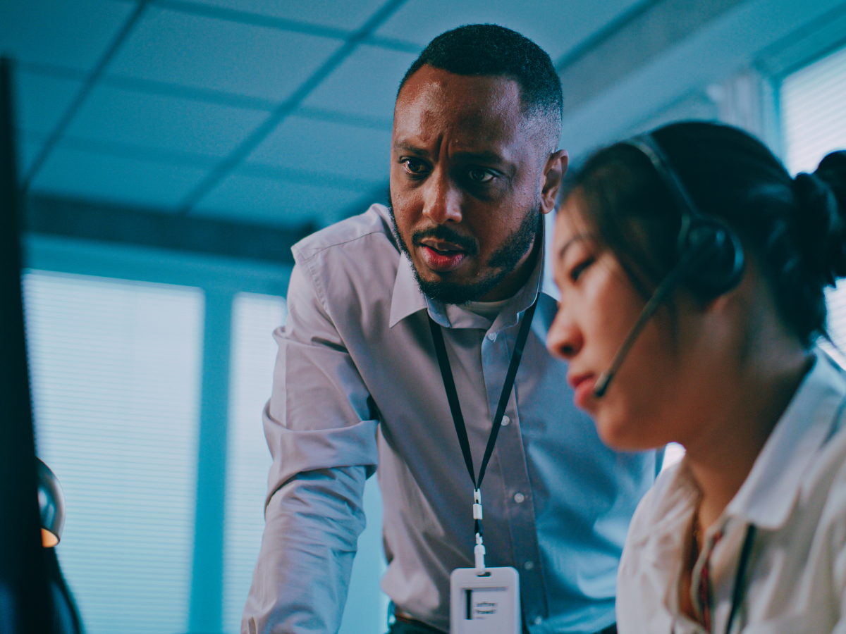 Supervisor at a distributed training firm looking over the shoulder of one of his colleagues with concern.