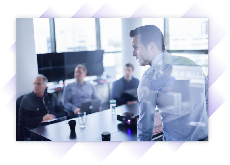 Business team in a boardroom meeting, attentively listening to a presenter with data projected on a screen.
