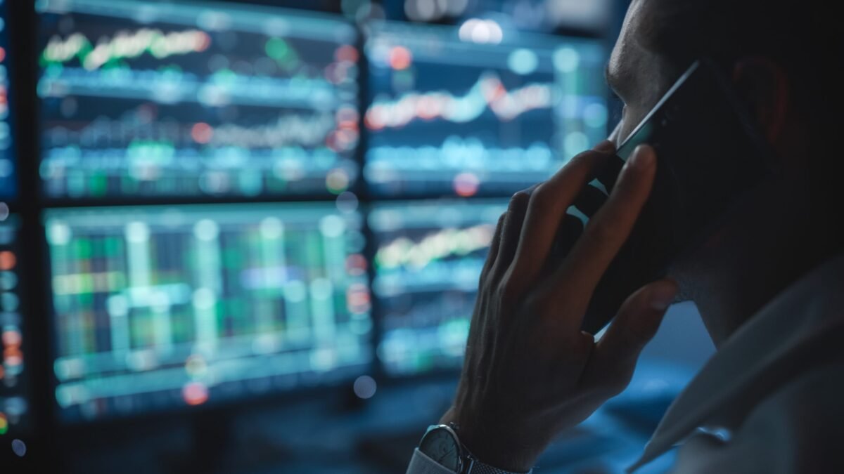 Financial analyst on the phone while looking at stock market dashboards.
