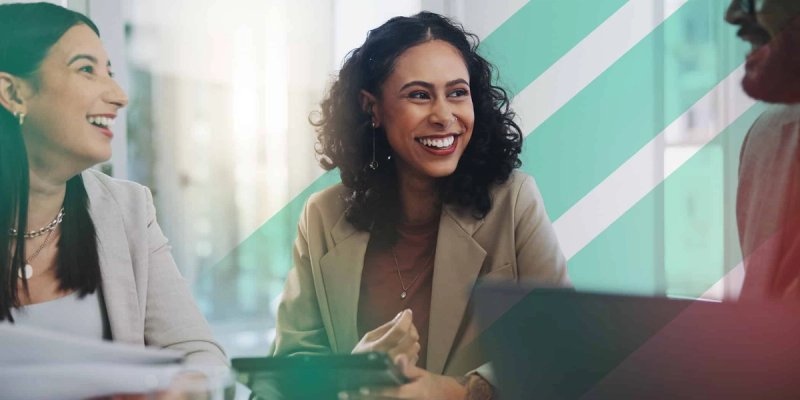 Two colleagues sit around a conference table with a customer success representative, smiling and laughing during a meeting in a brightly lit office.