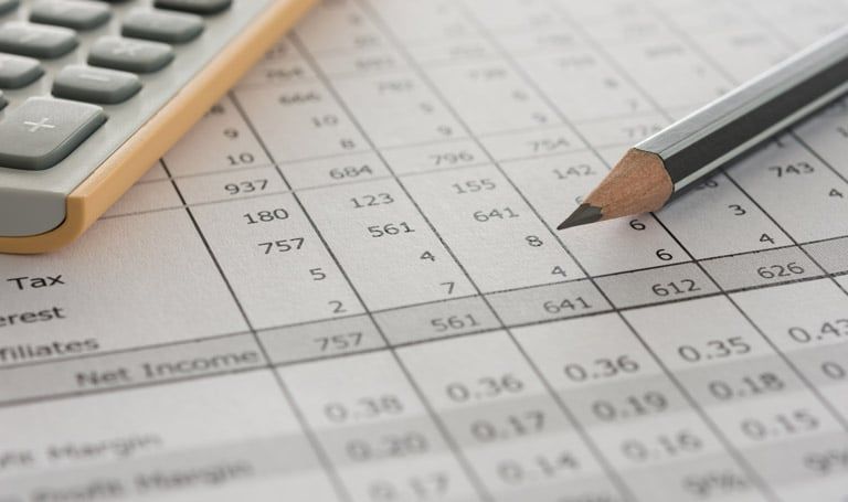 Close-up of a financial spreadsheet with a pencil and calculator, showing rows of numerical data including tax and net income figures.