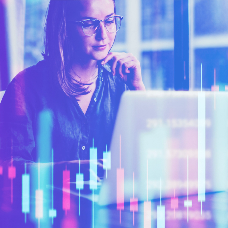 Woman with glasses working on a laptop overlaid with a translucent financial data visualization chart in blue and pink tones.