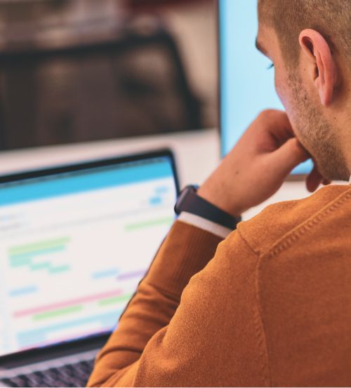 Man looking down at his laptop thoughtfully, with Administrate's AI Scheduler on the screen.