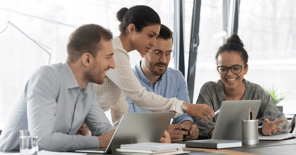 Training team in a boardroom with one member pointing at a laptop that they are all looking at.