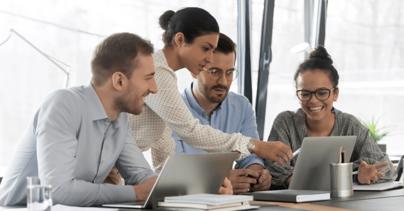 Training team in a boardroom with one member pointing at a laptop that they are all looking at.