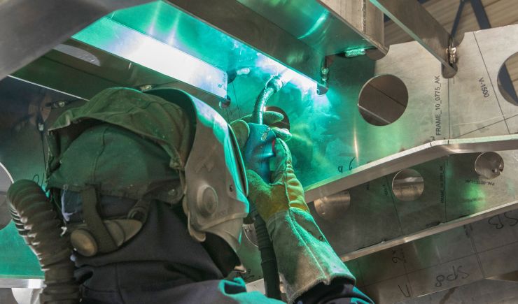 Worker inspecting the interior of a large industrial marine container, with equipment and coiled rope visible inside.