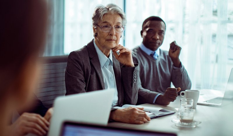 Training leaders gathered around their boss in a boardroom, looking concerned as they make a group decision.