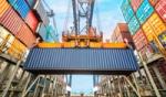 Yellow crane lifting a dark blue cargo container at a busy international shipping port terminal.