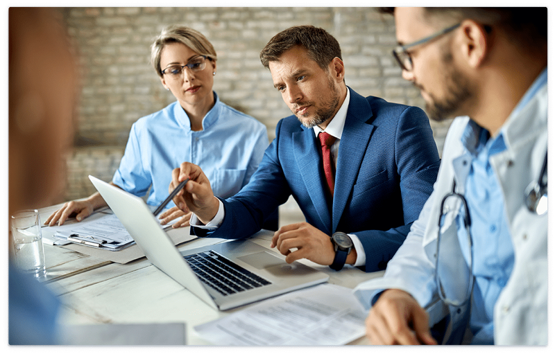 Meeting where business professional gesturing to laptop while a doctor and his colleague look on.