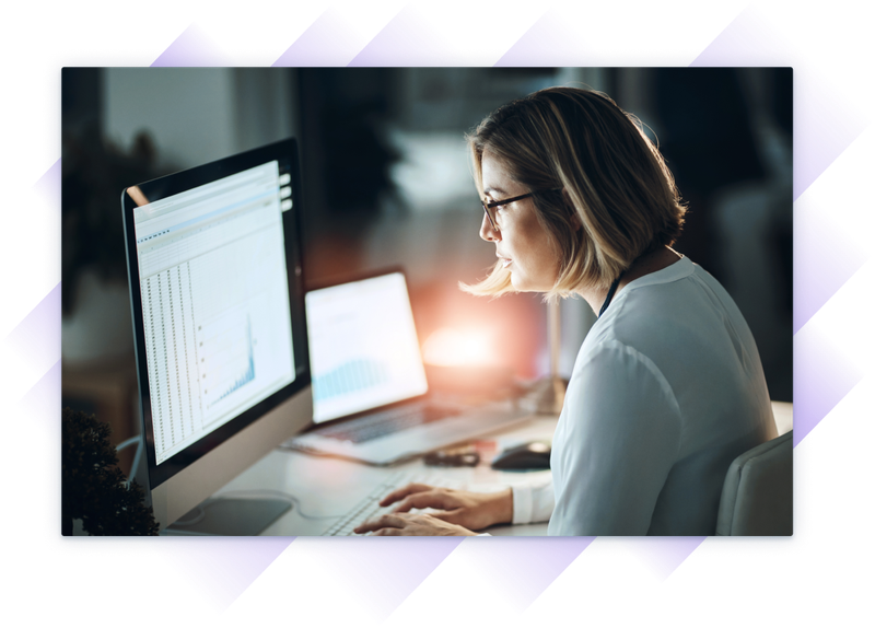 Woman looking closely at two monitors as the sun goes down.