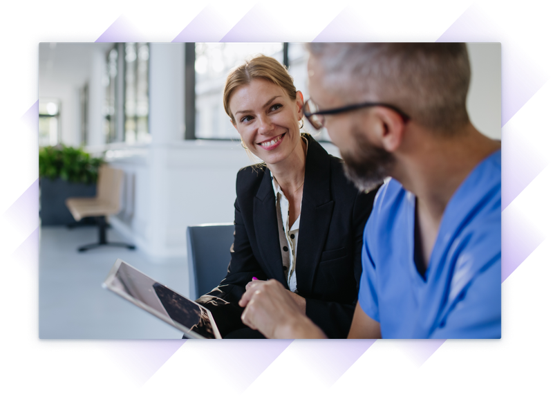 Smiling salesperson discussing something on a tablet with a medical worker in scrubs.