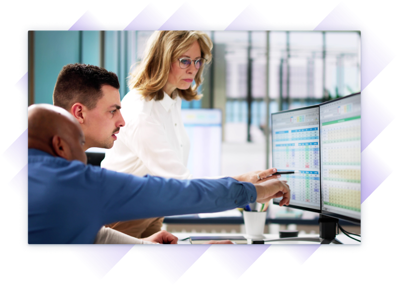 Three professionals review training data on dual monitors in a modern office.