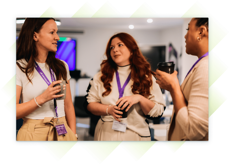Three female team members at our Customer Summit, chatting and holding coffee cups during a break, wearing Administrate lanyards.