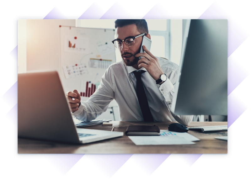 Very busy professional on a phone call while working on a laptop at a desk with charts and monitors.