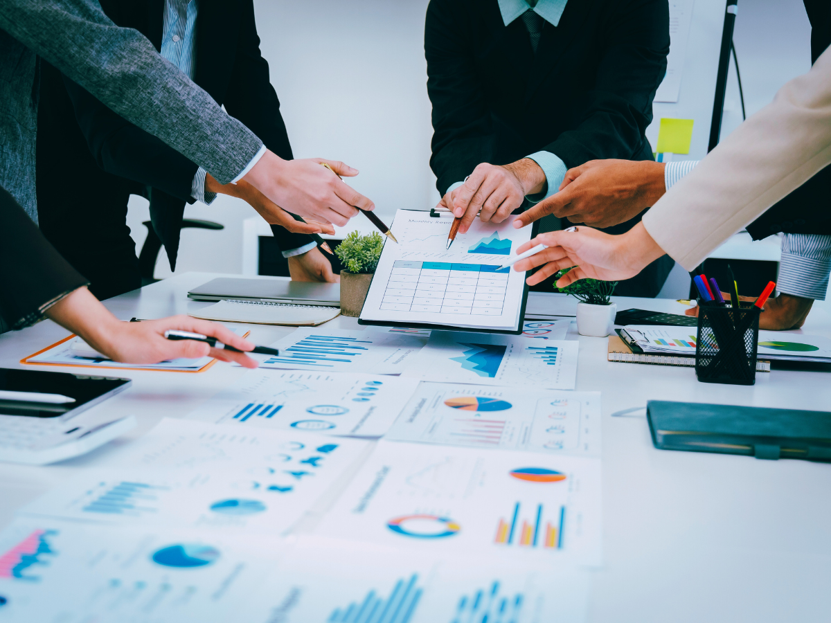 five hands pointing with pens at a clipboard