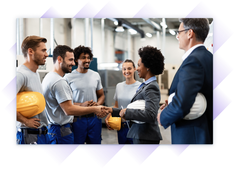 Female executive shaking hands with a factory worker in a group meeting with industrial staff.
