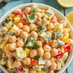 Chickpea and egg salad with diced vegetables, garnished with parsley, on a rustic table.