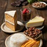 Five vegetarian desserts on a dark wooden table: a slice of two-layer carrot cake under off-white frosting, a glass of dark chocolate mousse topped with raspberries, a wedge of pale yellow key lime pie on a dark crumb crust, a pecan pie bar, and mango with sticky rice.