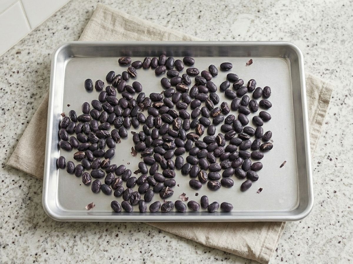 Black beans roasted dry in a single layer on a baking sheet, skins split open and matte.