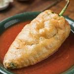 A Mexican chile relleno in a shallow green bowl, a whole poblano in puffed golden egg batter sitting in thin red tomato caldillo.