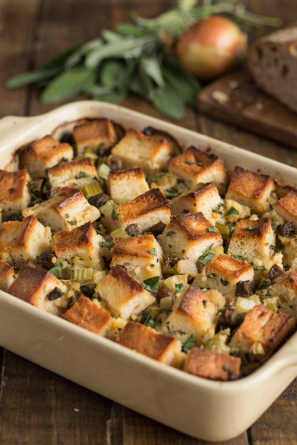 Vegetarian stuffing in a cream stoneware baking dish, cubes of sourdough with deep golden crisp tops over a soft herbed crumb, flecked with chopped browned mushroom, diced celery and fresh sage.