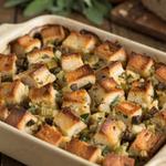 Vegetarian stuffing in a cream stoneware baking dish, cubes of sourdough with deep golden crisp tops over a soft herbed crumb, flecked with chopped browned mushroom, diced celery and fresh sage.