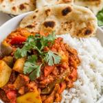 A bowl of spicy vegetarian vindaloo with colorful vegetables and cilantro, served with rice and naan.
