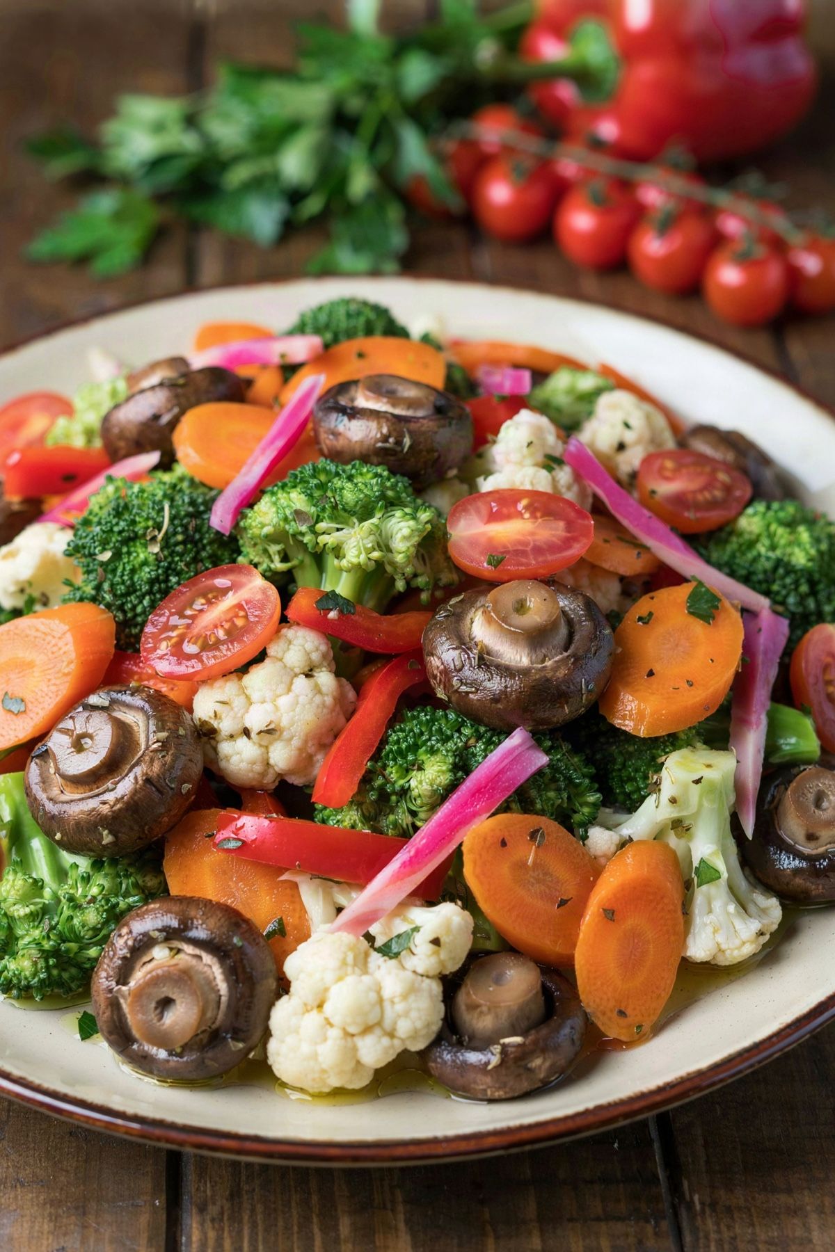 Marinated vegetable salad in a cream bowl: broccoli, cauliflower, carrot slices, dark marinated mushrooms, red pepper and pink pickled onion with halved cherry tomatoes