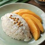 Thai mango sticky rice on a celadon plate, a mound of glossy coconut sticky rice under poured salted coconut cream with toasted mung beans, beside fanned slices of ripe golden mango.