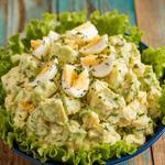 A creamy avocado and egg salad with avocado chunks and chopped eggs, garnished with herbs on lettuce leaves.