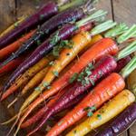 Roasted rainbow carrots glazed with honey, garnished with fresh herbs on a plate.