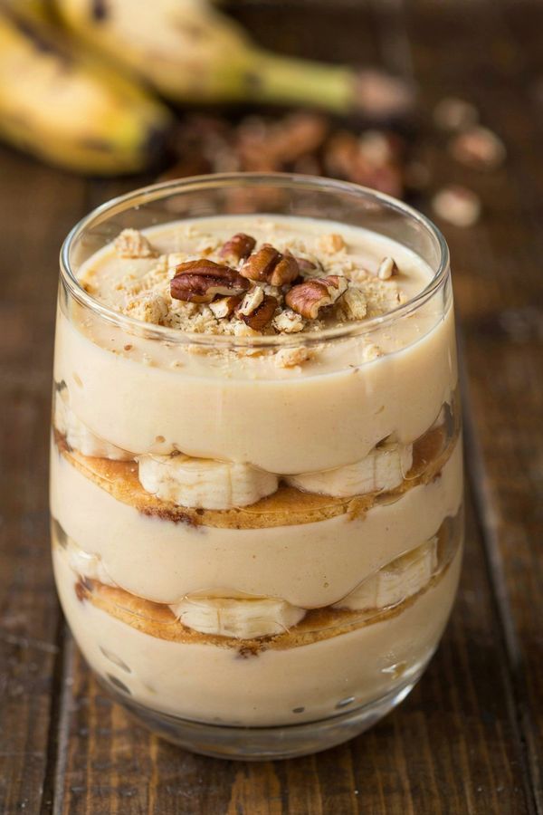 Vegan banana pudding layered in a glass, ivory pudding with banana slices and softened vanilla wafers under crushed wafers and toasted pecans