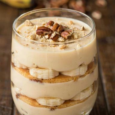 Vegan banana pudding layered in a glass, ivory pudding with banana slices and softened vanilla wafers under crushed wafers and toasted pecans