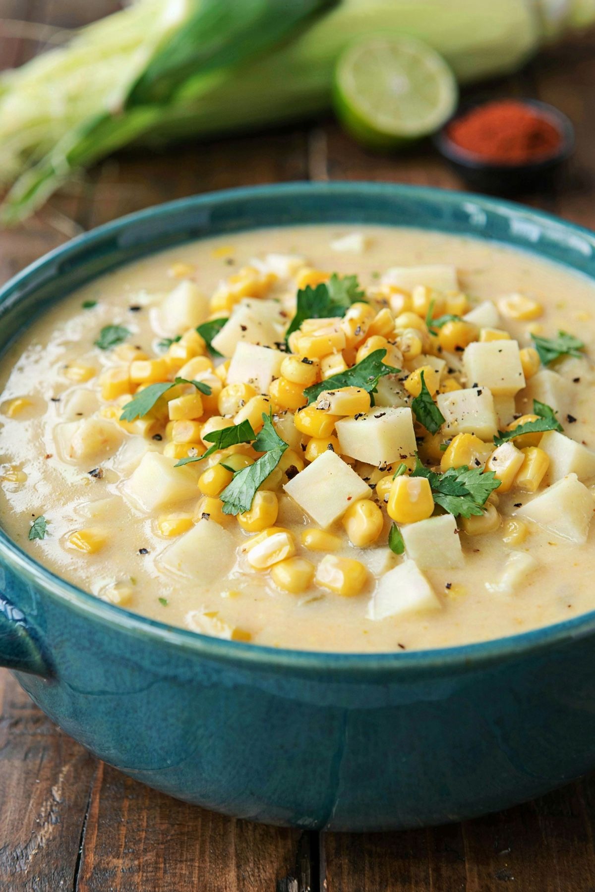 Vegan corn chowder in a teal bowl, thick and creamy with bright yellow corn kernels, diced potato, chopped cilantro and cracked black pepper.