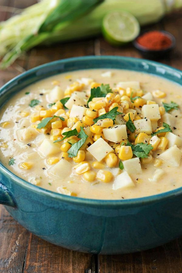 Vegan corn chowder in a teal bowl, thick and creamy with bright yellow corn kernels, diced potato, chopped cilantro and cracked black pepper.
