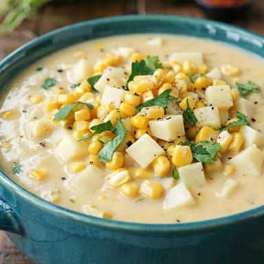 Vegan corn chowder in a teal bowl, thick and creamy with bright yellow corn kernels, diced potato, chopped cilantro and cracked black pepper.