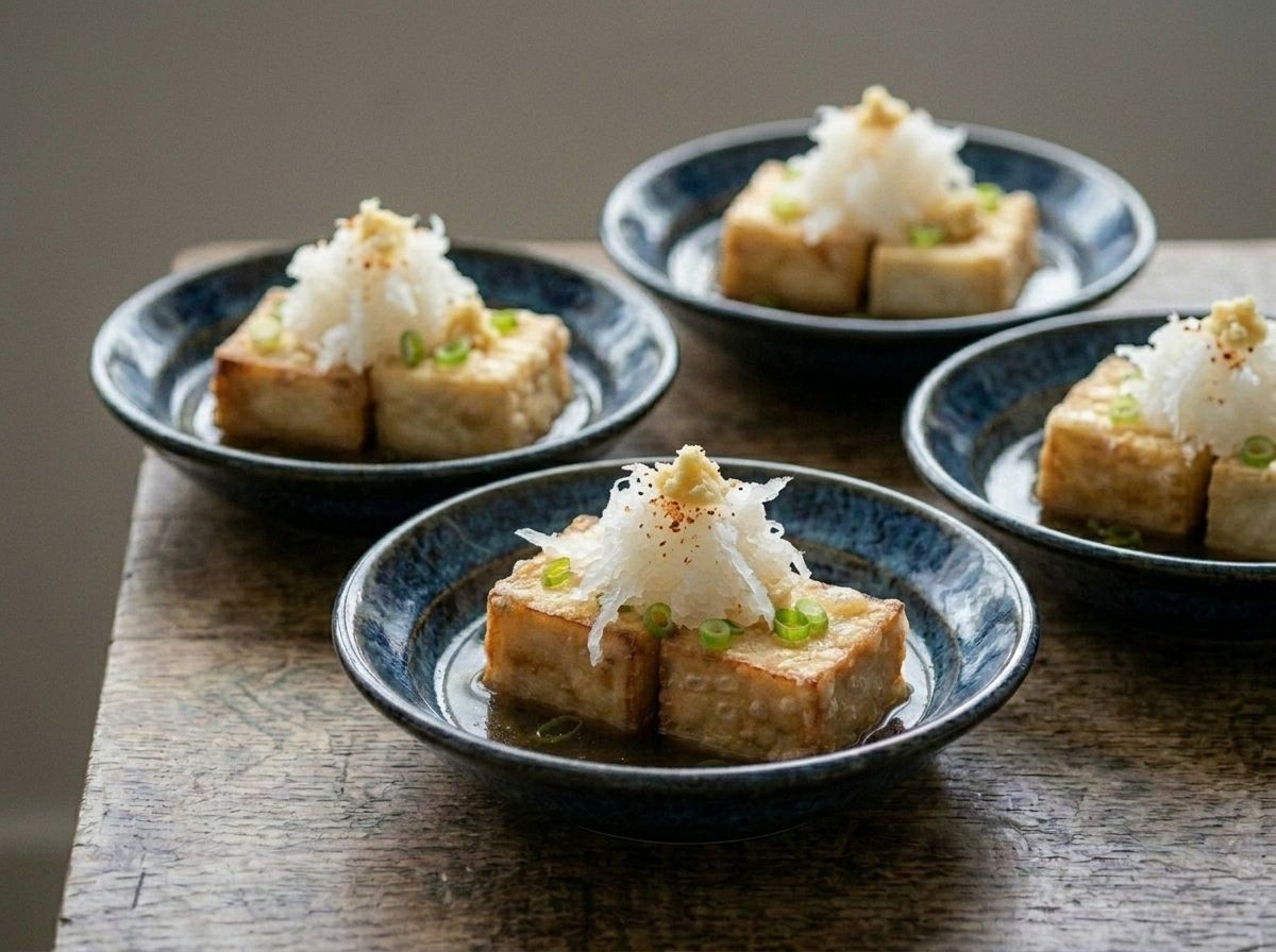 Four bowls of agedashi tofu standing in shallow dashi broth, each topped with grated daikon, ginger and scallion