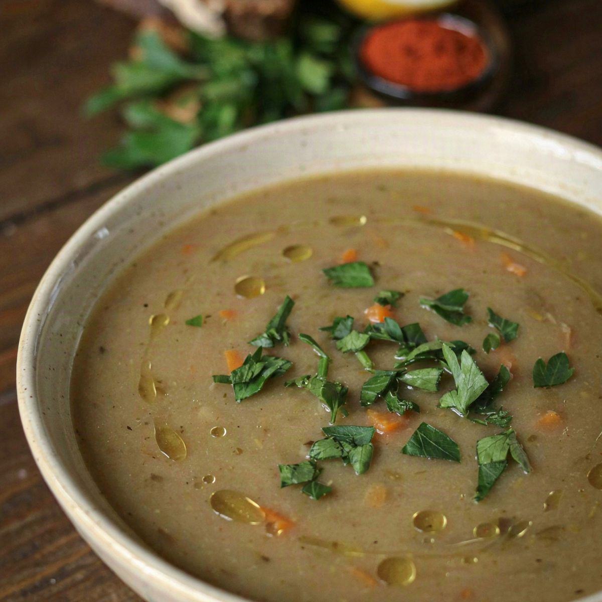 A bowl of thick meatless split pea soup, murky khaki green with flecks of carrot, scattered with chopped parsley and drizzled with olive oil, served with dark rye bread and a halved lemon.
