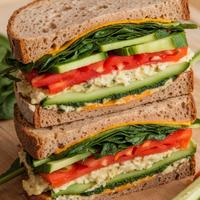 Vegetarian sandwich with mashed avocado, sliced tomato, cucumber, and red onion.