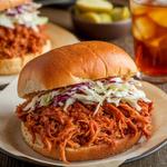 Vegan BBQ jackfruit sandwich with coleslaw and pickles on a bun.