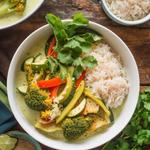 A bowl of vegan Thai green curry with vegetables in coconut milk, garnished with basil and cilantro, alongside jasmine rice.