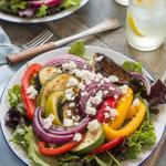 A vibrant Mediterranean roasted vegetable salad with bell peppers, zucchini, eggplant, and feta cheese on a wooden table.