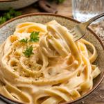 A bowl of vegan fettuccine Alfredo with cashew sauce and parsley garnish on a rustic table.