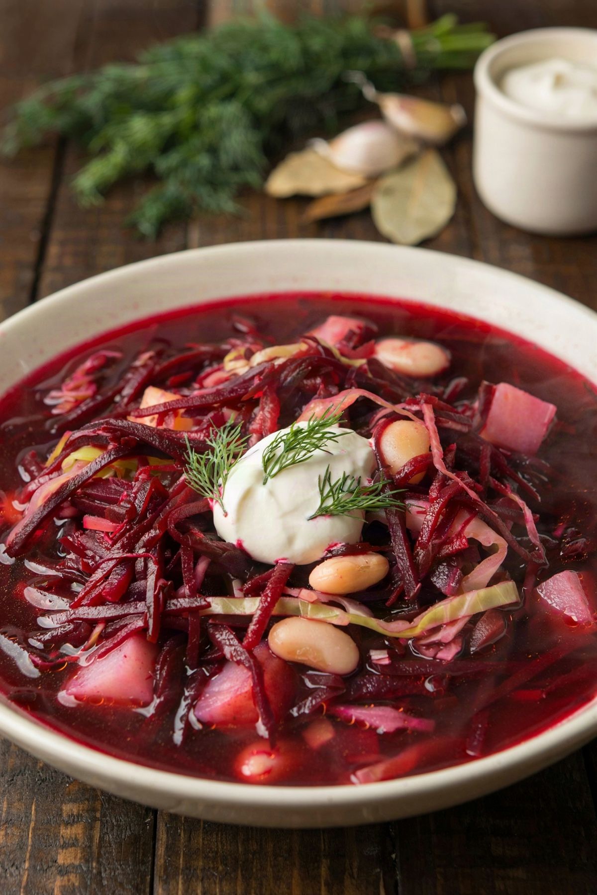 Vegetarian borscht in a cream bowl, a deep crimson soup of shredded beets, cabbage ribbons, potato and white beans, topped with sour cream and fresh dill.