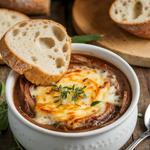 A bowl of vegetarian French onion soup with melted cheese and toasted bread, served on a rustic wooden table.