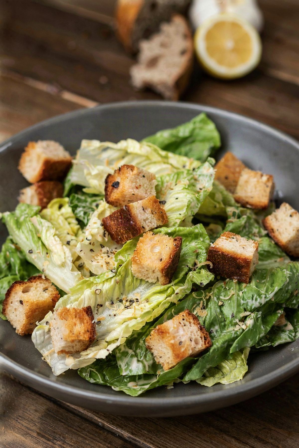 Vegan Caesar salad in a gray stoneware bowl, romaine tossed in creamy cashew dressing with golden sourdough croutons, nutritional yeast flakes and cracked black pepper