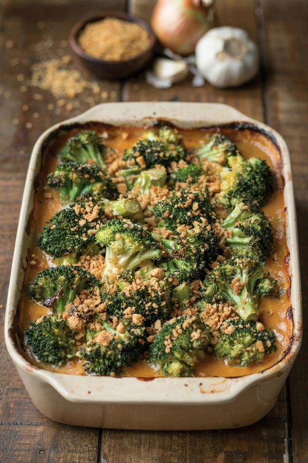Vegan broccoli casserole in a cream stoneware baking dish, roasted broccoli florets with browned tips coated in a thick orange-gold sauce under a scattered layer of golden buttery cracker crumbs.