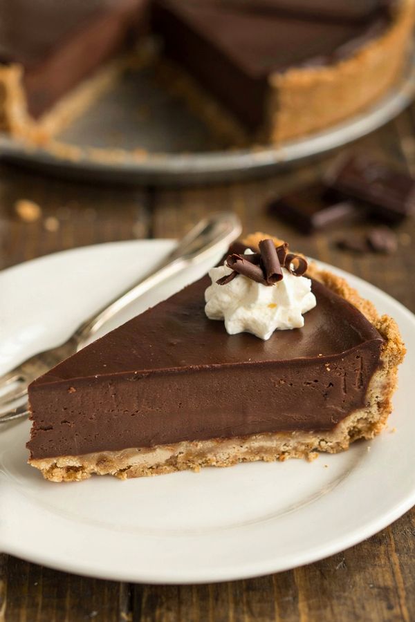 A slice of silken chocolate pie on a white plate, a dense dark chocolate layer on a graham cracker crumb base, topped with whipped cream and dark chocolate curls