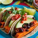 Tacos filled with sweet potatoes, black beans, garnished with cilantro, and served with lime wedges.