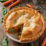 A freshly baked vegetarian pot pie with a flaky crust and colorful vegetable filling on a rustic table.